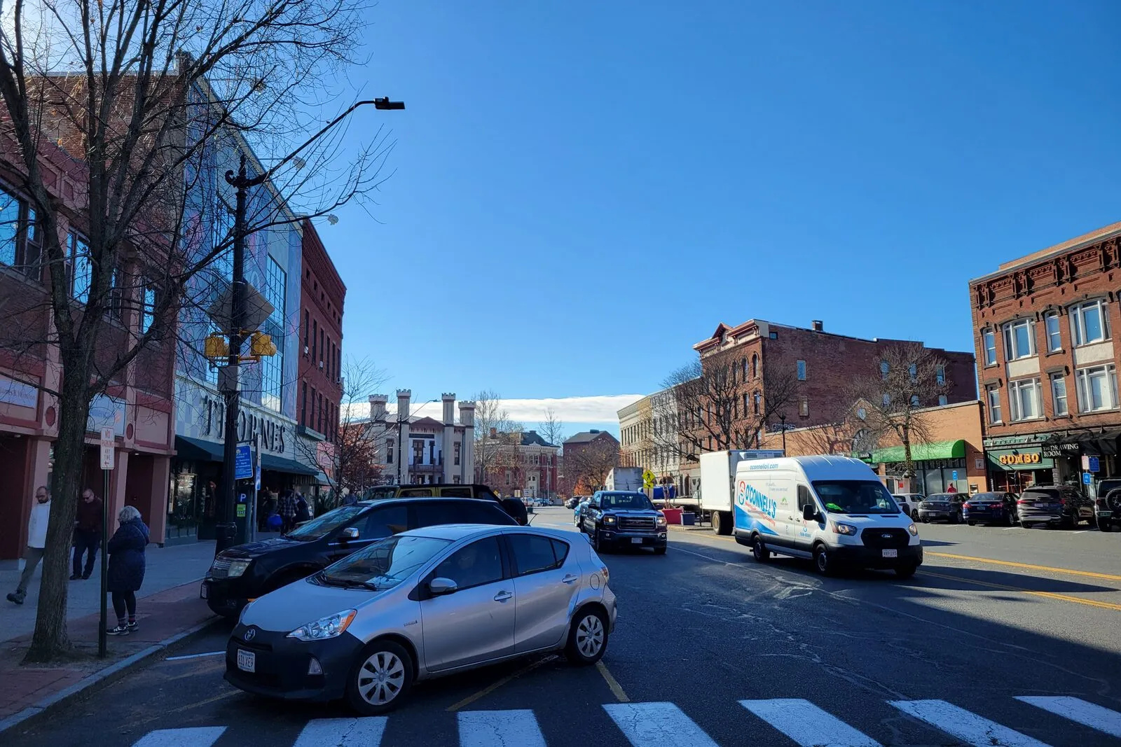 Main Street in downtown Northampton under a clear winter sky: Thornes Marketplace on the left, a row of three- and four-story brick commercial buildings on the right, and the towered Hampshire County Courthouse rising in the distance at the end of the street.